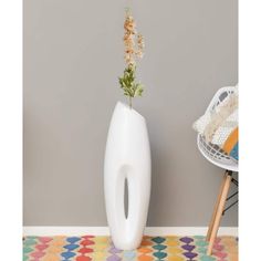 a white vase sitting on top of a colorful rug next to a wall with a plant in it