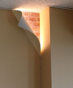 the corner of a room with a light coming from it's ceiling and a brick wall