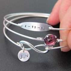 a person is holding two silver bracelets with a pink stone on it and the word mom written in arabic