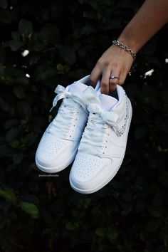 a person's hand holding onto a pair of white sneakers