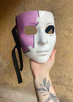 a person holding up a white mask with purple and black designs on it's face