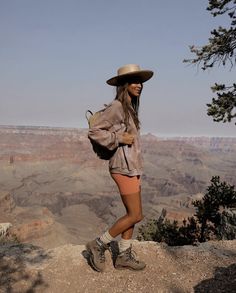 a woman standing at the edge of a cliff with her back to the camera and wearing a hat