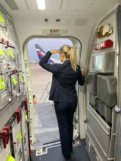 a woman standing in the doorway of an airplane looking out at the runway and taking off