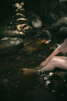 a woman sitting in the water with her legs crossed and feet spread out on rocks