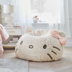 a hello kitty bean bag chair with a bow on the front and side, in a bedroom