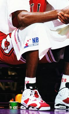 a basketball player is sitting on the court with his foot up to his knee and wearing white shoes