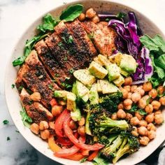 a white bowl filled with meat, vegetables and chickpeas on top of a marble table