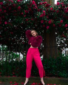 a woman standing in front of a tree with roses on the ground and her arms behind her head