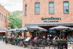 people sitting at tables in front of a building with umbrellas on the outside patio