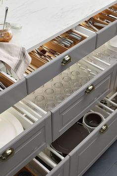 an open drawer with silverware in it and coffee mugs on the counter top