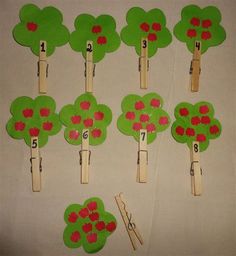 several green trees with red apples on them are cut out from clothes pins and placed on a white surface