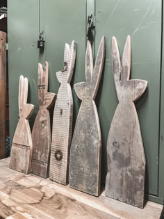 several wooden rabbits are lined up against a green wall in front of a wood table