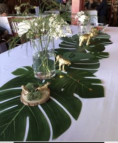 the table is set up with green leaves and vases filled with white flowers, small giraffe figurines on each side