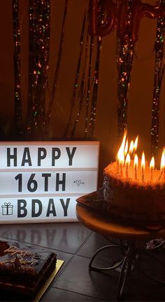 a birthday cake with lit candles sitting on a table next to a sign that says happy 16th birthday