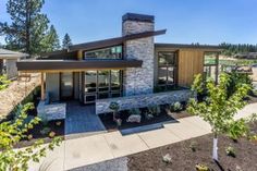 a modern house with stone and wood accents in the front yard, surrounded by trees