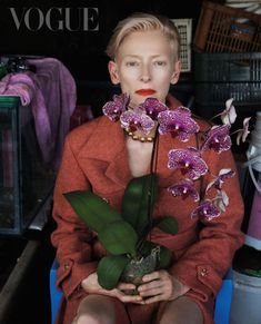 a woman sitting in a chair holding a vase with purple flowers on top of it