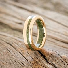 a gold wedding ring with green wood inlays on it's side sitting on a piece of wood