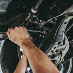 a man is working on the underside of a car's front wheel and suspension