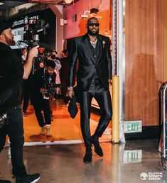 a man in a black suit and sunglasses walking into a building with cameras around him