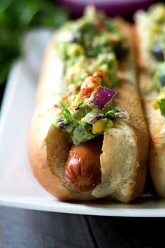 two hotdogs with condiments on them sitting on a white platter