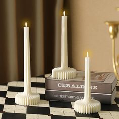 two white candles sitting on top of a black and white checkered table