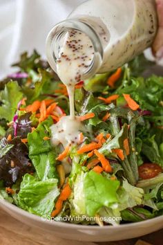 dressing being poured onto a salad in a bowl with lettuce and carrots