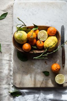 a wooden bowl filled with oranges and lemons on top of a white table