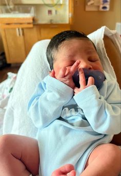 a baby laying on top of a bed holding a cell phone to its ear and mouth