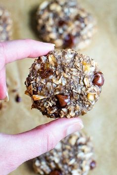 a hand holding a cookie with nuts and raisins on it in front of other cookies