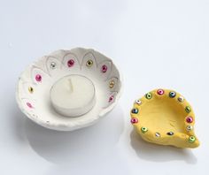 a white candle holder next to a ceramic bowl filled with beads and a lit candle