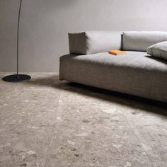 a grey couch sitting on top of a floor next to a lamp and a table