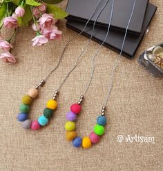 three necklaces with different colored beads are sitting on a table next to some flowers