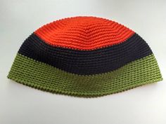 a crocheted hat with an orange and black stripe on the top, sitting on a white surface