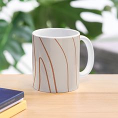 a coffee cup sitting on top of a wooden table next to a book and plant