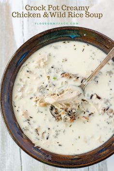 a bowl of chicken and wild rice soup with a spoon in it on a white wooden table