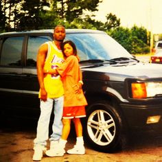 a man and woman standing in front of a black suv with their arms around each other