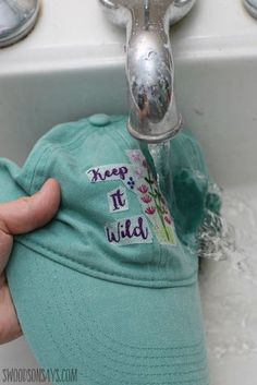 someone is holding their hat in front of the faucet