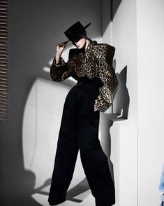 a woman in leopard print shirt and wide legged black pants posing for a magazine cover