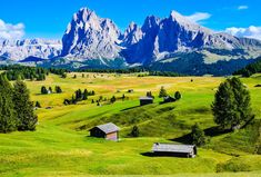 the mountains are covered in green grass and there is a small cabin on the far side