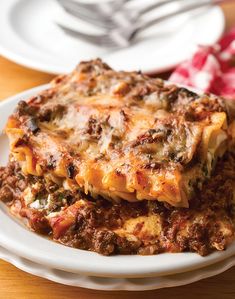 a white plate topped with lasagna covered in cheese and sauce on top of a wooden table