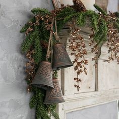 three bells are hanging on the wall next to a wreath with pine cones and greenery