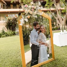 a bride and groom are standing in front of a mirror with flowers on it at their wedding