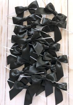 several black bows are tied together on a white wooden surface with pins attached to them