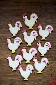 twelve decorated cookies in the shape of chicken's on a wooden table with white icing