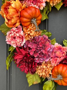 a wreath made out of fake flowers and pumpkins on a gray door with green leaves