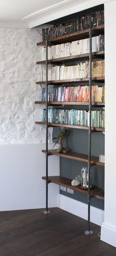 a bookshelf filled with lots of books next to a white wall and wooden floors