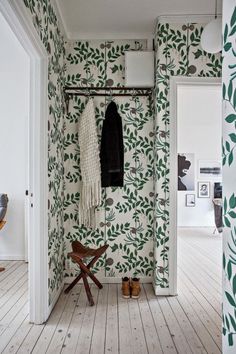 a white and green wallpapered room with a coat rack on the wall next to a wooden bench