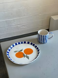 two oranges on a blue and white plate next to a cup