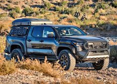 a black truck is parked in the middle of some brush and rocks on a sunny day