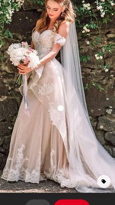 a woman in a wedding dress standing next to a stone wall with flowers on it